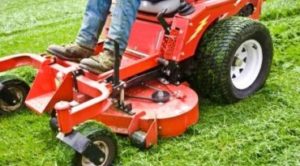 man on a riding lawn mower that has grass stuck to the wheels. spring and summer outdoor maintenance.